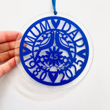 Beautiful sapphire blue glass hanging ornament celebrating a 45th wedding anniversary. Features "Mum & Dad," two lovebirds, floral design, and the years 1980–2025 in an elegant cut-out style. Shown hanging in a bright home interior, perfect as a keepsake or window decoration for a special milestone.